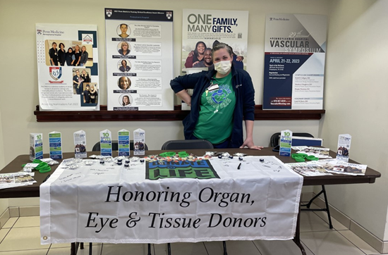 Kate DiMedio stands behind a table with a banner on the front scribed with Honoring Organ, Eye and Tissue Donors